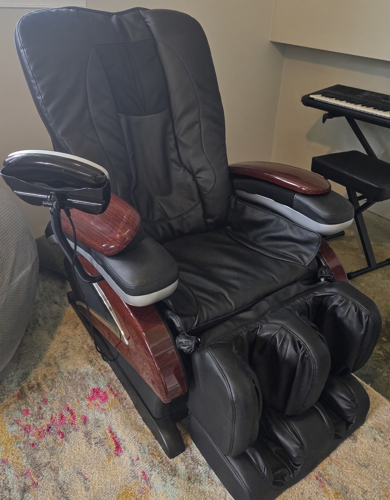 Black shiatsu massage chair angled toward keyboard on patterned rug